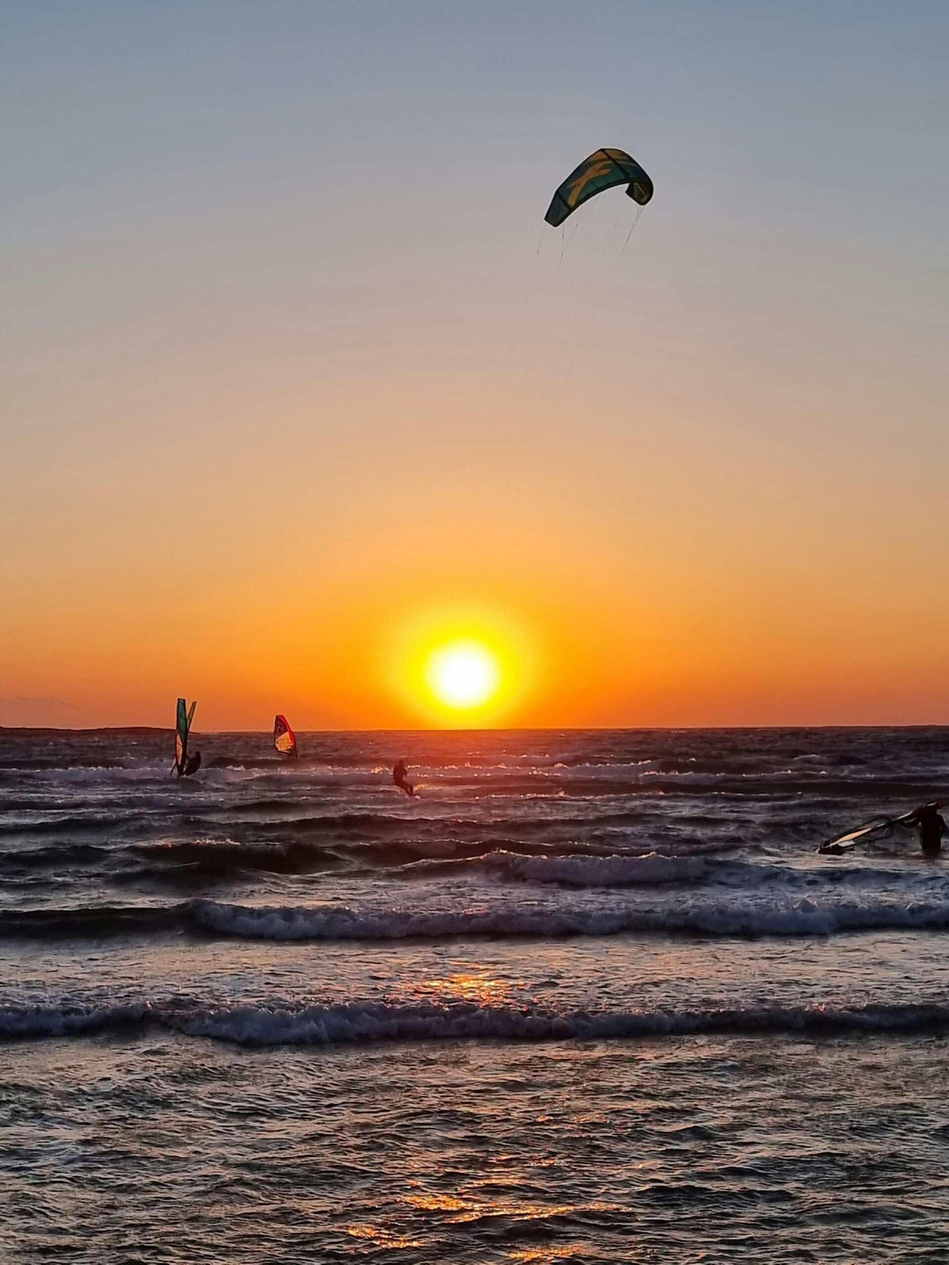 Kitesurfers catch waves against a vibrant sunset in Rhodes, Greece, capturing the thrill of water sports.