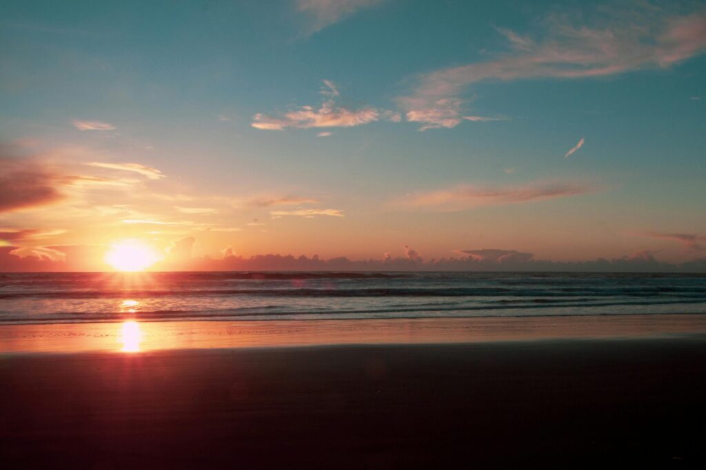 A tranquil beach sunset with vivid colors reflecting on the sand and sea, capturing a peaceful seascape.